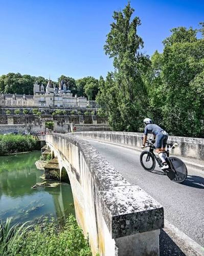 Kolarz przejeżdżający przez most z zamkiem w dolinie Loary podczas Ironman Tours